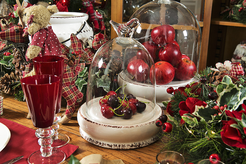 Frutas vermelhas, como cerejas e maças, tomam parte da decoração da mesa, em pratos de cerâmica artesanal com tampa de vidro. A lanterna de cerâmica Flower, decorada com festão e flores de tecido, ilumina a refeição.