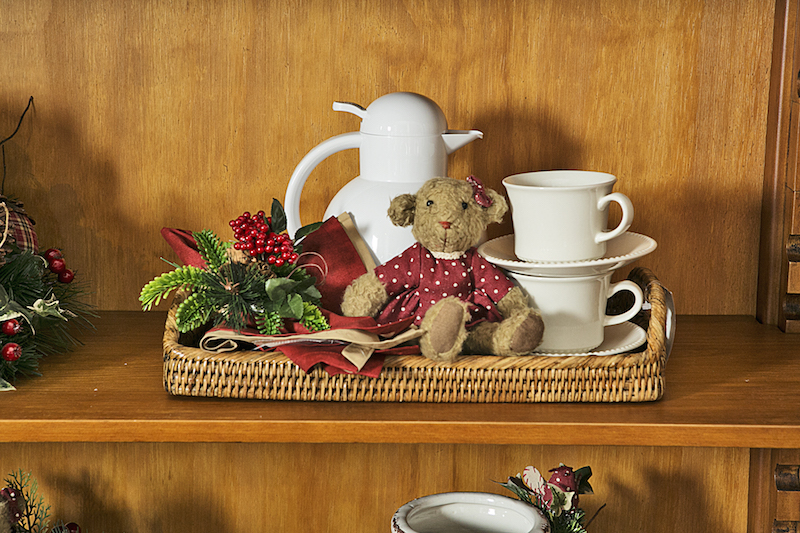 A bandeja, pronta para o chá, deixa disponíveis as xícaras e os guardanapos com enfeites de ramos natalinos. Tudo guardado pela ursa de vestido.