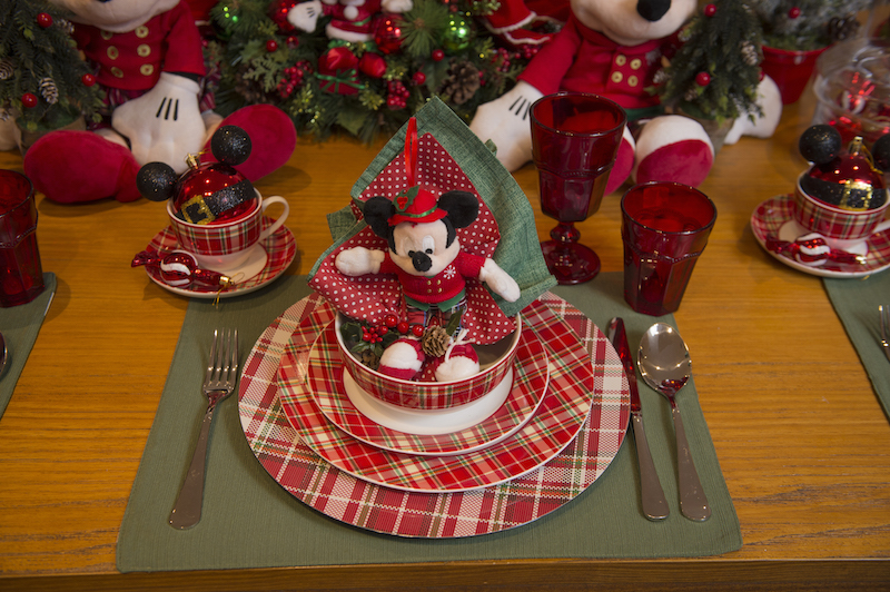 No lugar reservado para cada criança, várias surpresas os esperam. A primeira é o Mickey ou a Minnie sentados no bowl xadrez, servindo de porta-guardanapos. Copos vermelhos de vidro para o suco e o leite batido com chocolate. A louça xadrez Forest combina com as calças do Mickey, que veio muito elegante para festa de Natal.