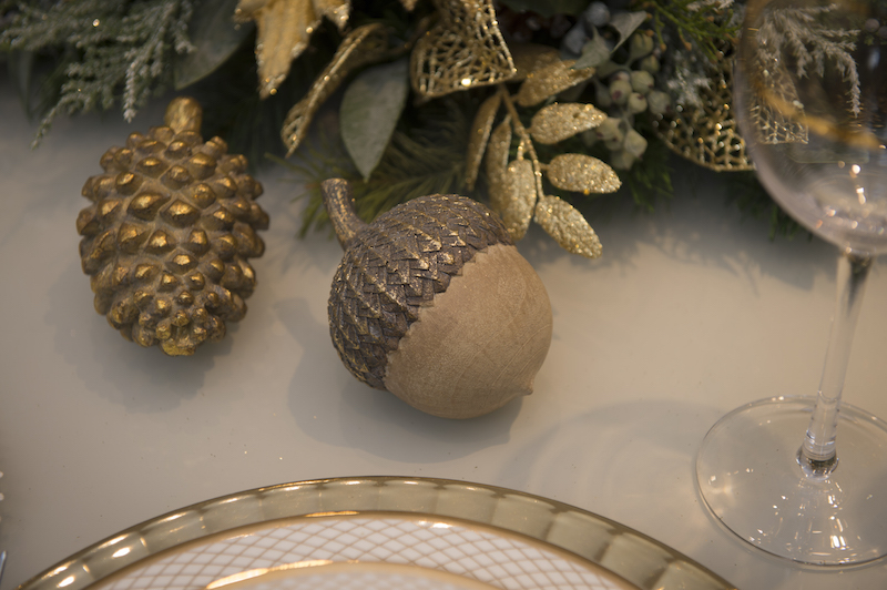 Pinha e avelã em madeira com patina dourada compõem a decoração da mesa da ceia de Natal.