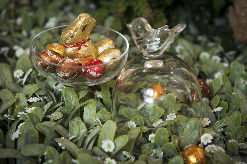 Em meio ao verde, o prato de pé com tampa Bird, em vidro, serve de ninho para um coelho mini de chocolate (Lindt) e mini-ovinhos de vários sabores.